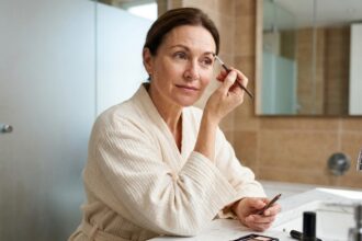 Femme mature redessinant ses sourcils clairsemés avec un crayon à sourcils devant un miroir de coiffeuse