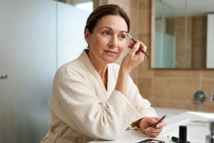 Femme mature redessinant ses sourcils clairsemés avec un crayon à sourcils devant un miroir de coiffeuse