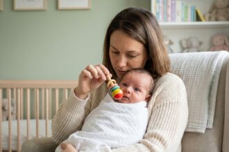 Mère tenant son nourrisson et stimulant son suivi visuel avec un hochet coloré dans une chambre de bébé moderne